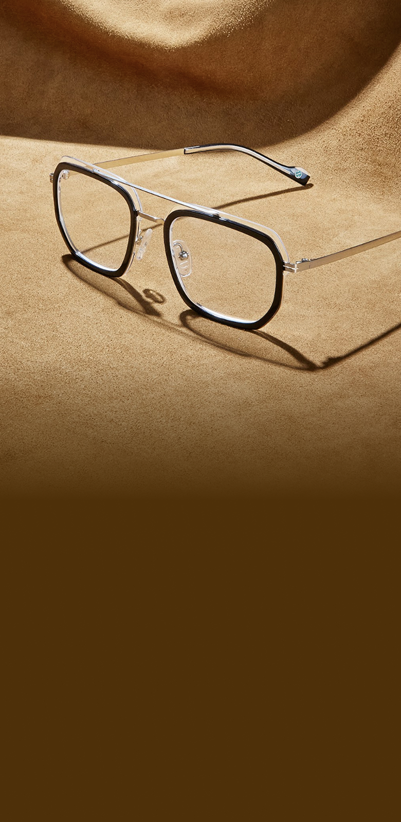 Square black and silver aviator glasses on a brown suede surface.