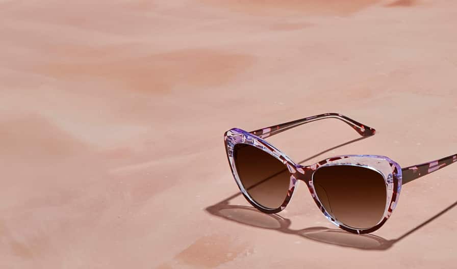 Lentes estilo ojo de gato, modelo Zenni número 115417, apoyados en forma oblicua contra una esfera de piedra beige sobre un fondo neutro.