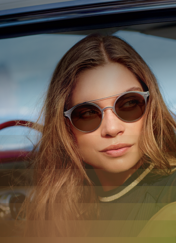 A woman with long brown hair wearing light-adaptive Transitions® sunglasses, which darken in bright sunlight.