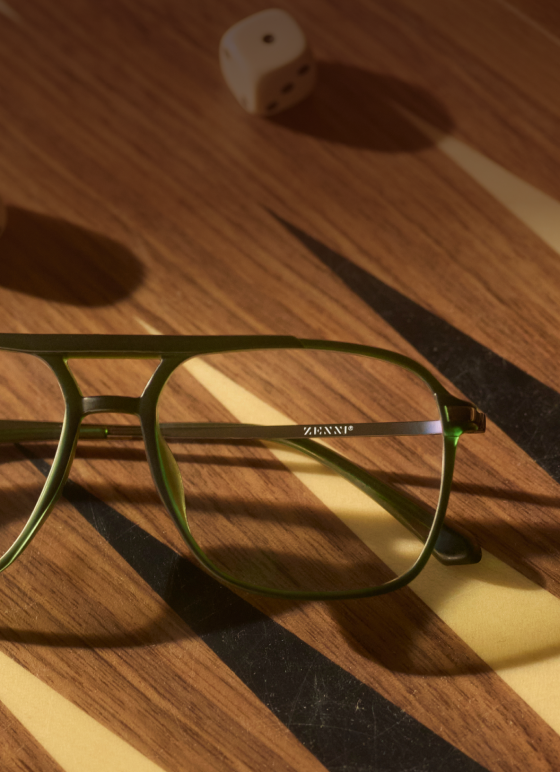 Close-up of a pair of green-framed Zenni Progressive glasses lying on a wooden backgammon board.