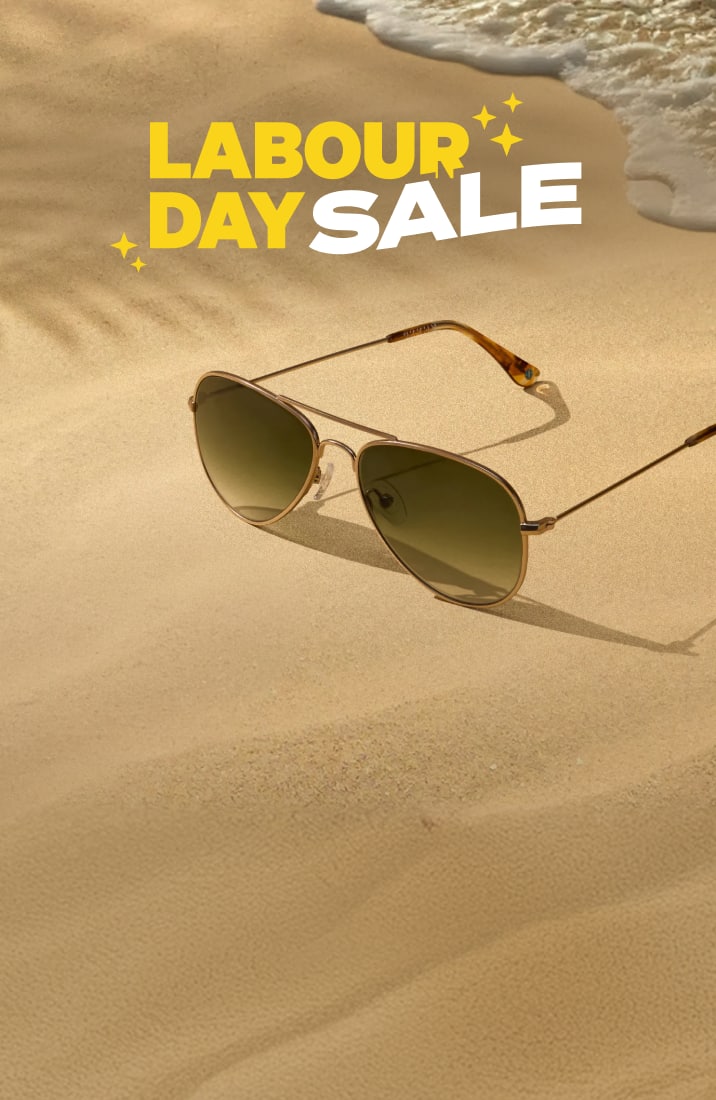Two pairs of aviator sunglasses resting on sandy beach shore with ocean waves, beneath bold text reading LABOUR DAY SALE.