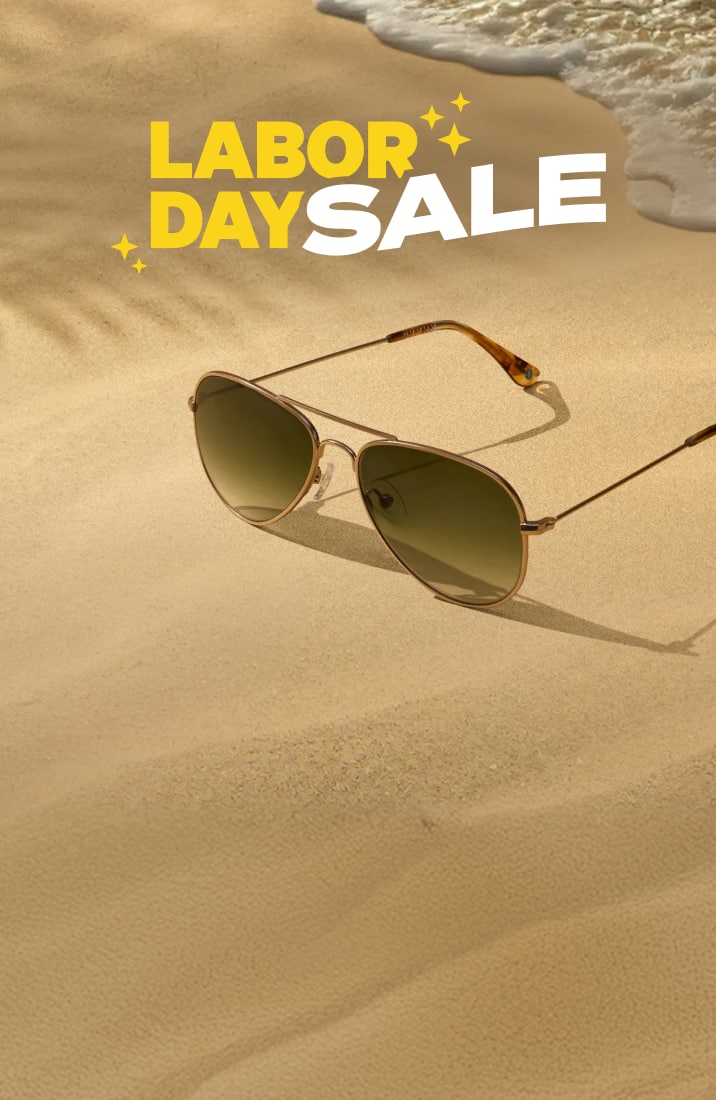Two pairs of aviator sunglasses resting on sandy beach shore with ocean waves, beneath bold text reading LABOR DAY SALE.