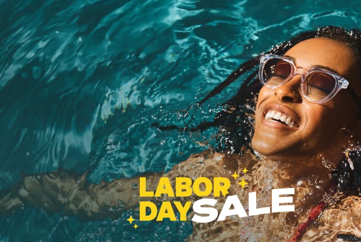 A woman with black locs wearing clear square Zenni sunglasses smiles as she tips her head back in a pool. Additional text: Labor Day Sale in wavy all-caps white and yellow type.