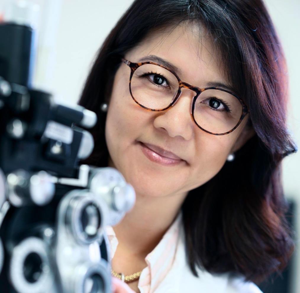 Image of an optician wearing a pair of Zenni glasses, behind a phoropter.