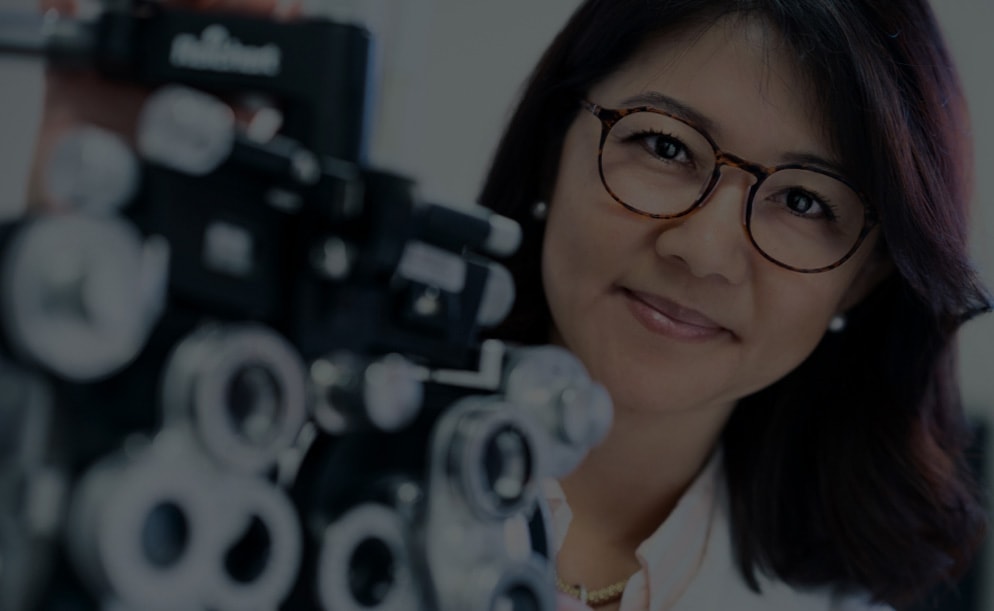Image of an optician wearing a pair of Zenni glasses, behind a phoropter.