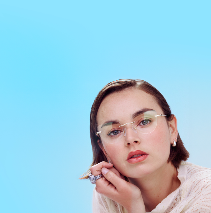 Close-up of a woman in a tan top against a blue background wearing Zenni rimless glasses.