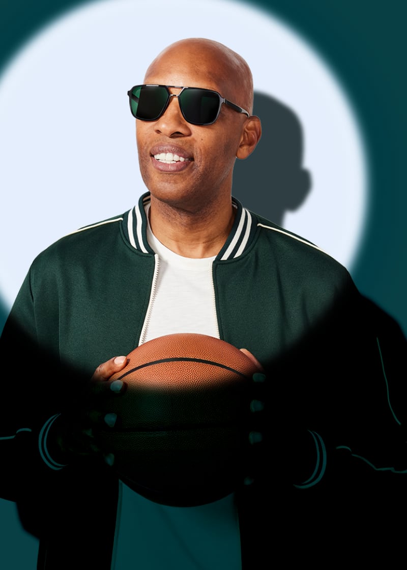 Sam Cassell holding a basketball while wearing dark rectangular sunglasses in a spotlight against a deep teal background.
