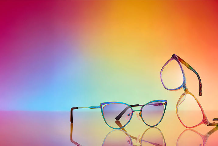 Rainbow metal cat-eye sunglasses and rainbow sparkle plastic square glasses on a rainbow background.