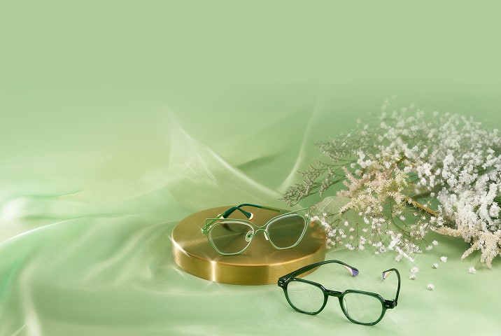Green geometric Zenni glasses on a gold pedestal and dark green Zenni glasses on green satin.