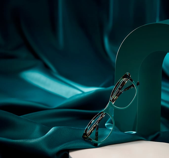 Tortoiseshell and teal mutlicolor Zenni glasses on a teal satin background.