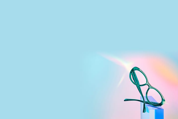 Translucent green eyeglasses on a small blue block with a pastel gradient background.
