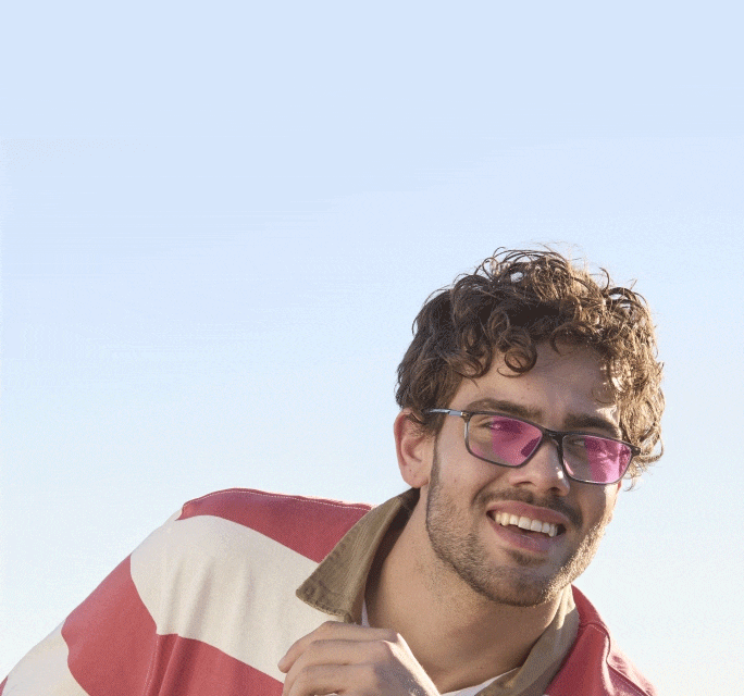 An animated lifestyle shot of a man wearing rectangular glasses; the lenses transition from clear to a vibrant pink tint, demonstrating a light-reactive or clarity-enhancing lens feature.