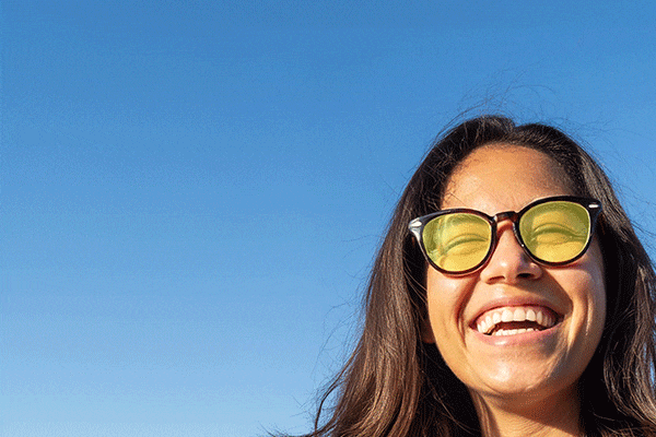 Woman with long hair and big smile wearing Zenni round glasses with sunglasses tint different colors.
