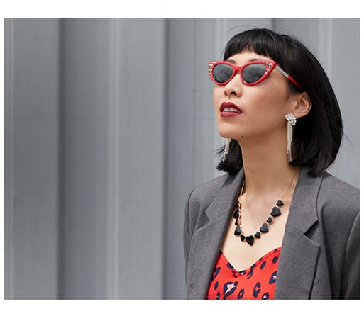 Woman with edgy black bob and red lipstick wears extreme red cat-eyes with silver studs #7820918 with dark gray Blokz tinted lenses and a gray blazer over a red leopard-print top.