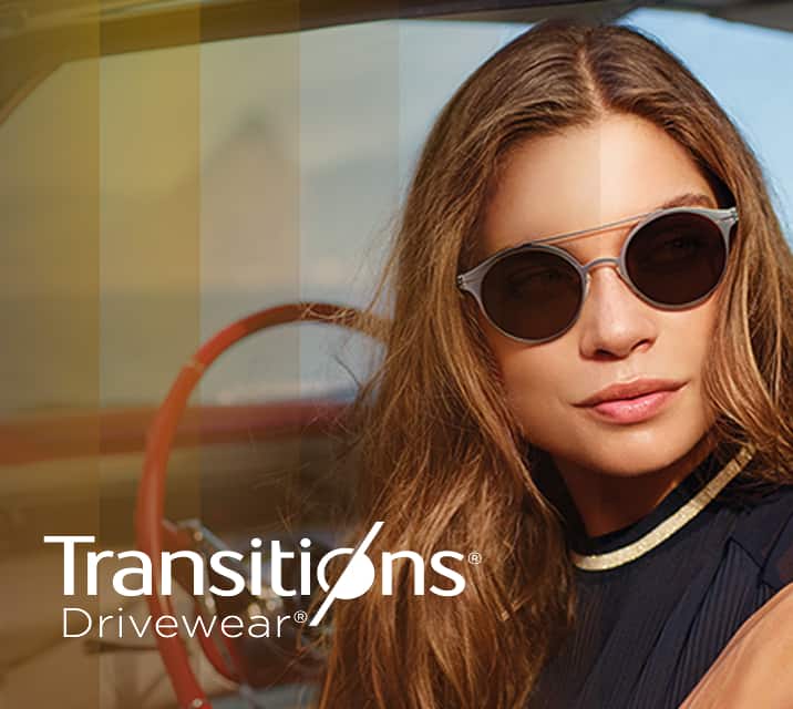 A woman sitting in the front seat of a car wearing round glasses with Transitions lenses that change from dark to darker.