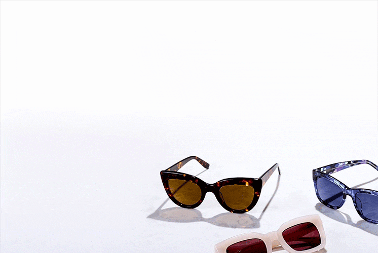 Three pairs of sunglasses sit on a light surface: one with a tortoiseshell cat-eye frame and amber lenses, one with pearl square frames and red lenses, and one with a marbled blue rectangular frame and blue lenses.