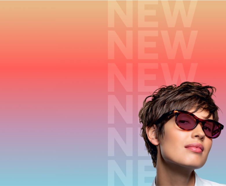 A woman in tortoiseshell glasses with ruby red Transitions Gen S lenses that change from clear to dark.