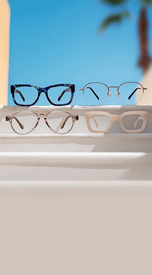 Pink rectangle glasses with ruby red lenses, round metal glasses with emerald green lenses, multicolor tortoiseshell glasses with amethyst purple lenses, and beige aviator glasses with sapphire blue lenses, on a white ledge with blue sky and a palm tree in the background.