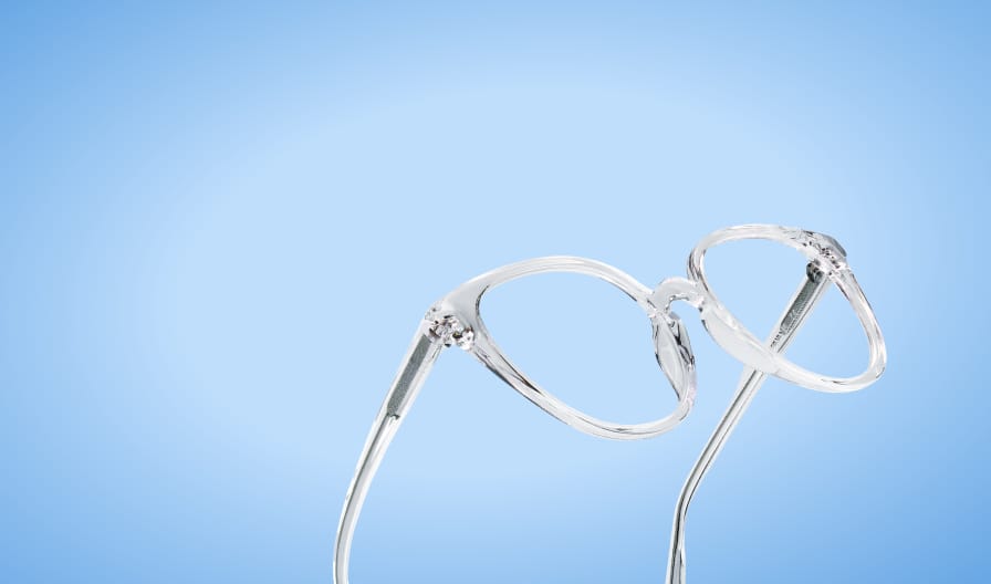 Clear translucent round eyeglasses angled upward against a soft blue gradient background.
