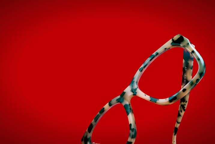 Close-up of light blue and cream tortoiseshell cat-eye eyeglasses angled vertically against a vivid red background.