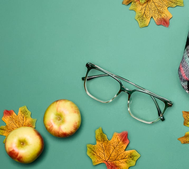 Green ombre square glasses on a green background with apples, fall leaves, and a plaid scarf.