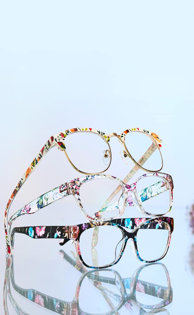 Stacked floral Zenni eyeglass frames in vibrant colors on a reflective surface.
