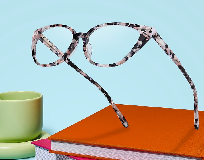 Gafas tipo ojo de gato Zenni estampadas sobre un escritorio colorido con libros y una taza.