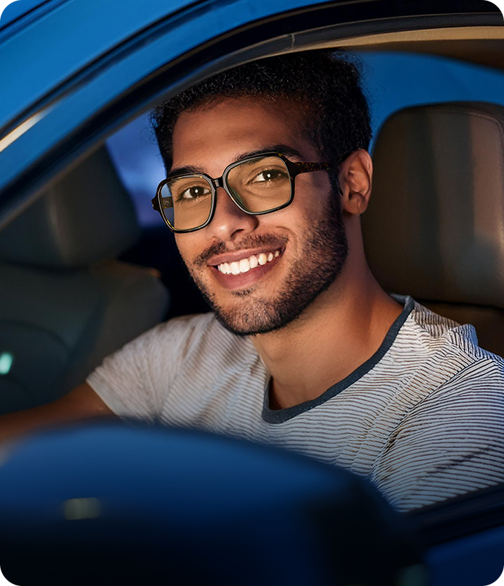 Persona sonriente con Lentes Zenni mientras está sentada en un auto por la noche.