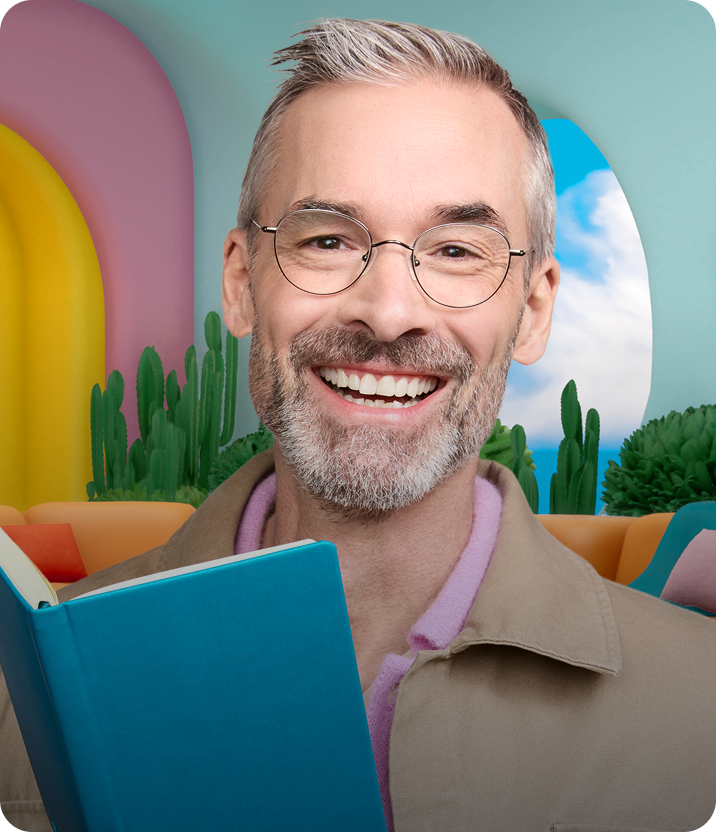 Persona sonriente con Lentes Zenni redondas de alambre y un libro en una habitación colorida.