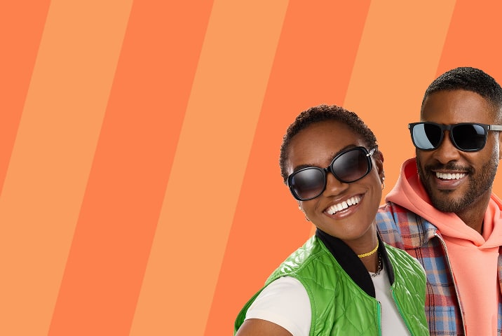 Two smiling people side-by-side against an orange diagonally striped background; a woman with short hair wears oversized black sunglasses and a green vest, next to a man wearing black square sunglasses.