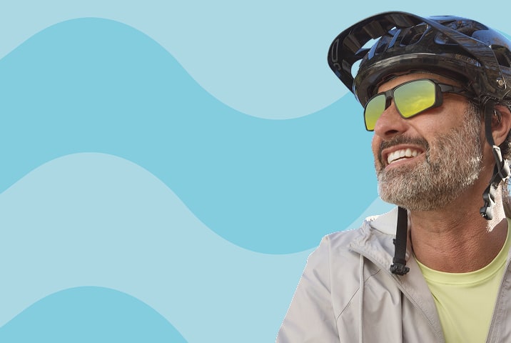 A man with a salt and pepper beard wearing black rectangle Zenni sports sunglasses with yellow mirror lenses. Blue wavy stripe background.