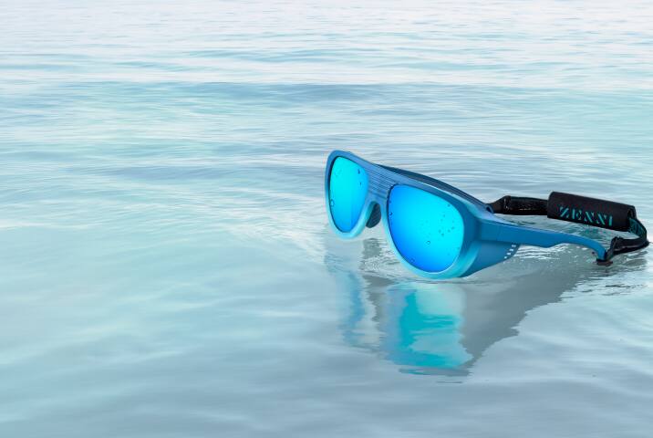 Lentes de sol para deportes acuáticos azules con cristales espejados azul vibrante y correa negra flotando sobre agua azul clara.
