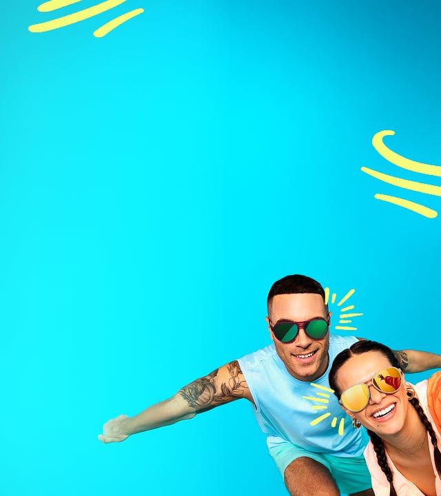 Man and woman smiling and taking a selfie in colorful sunglasses against a bright blue background.