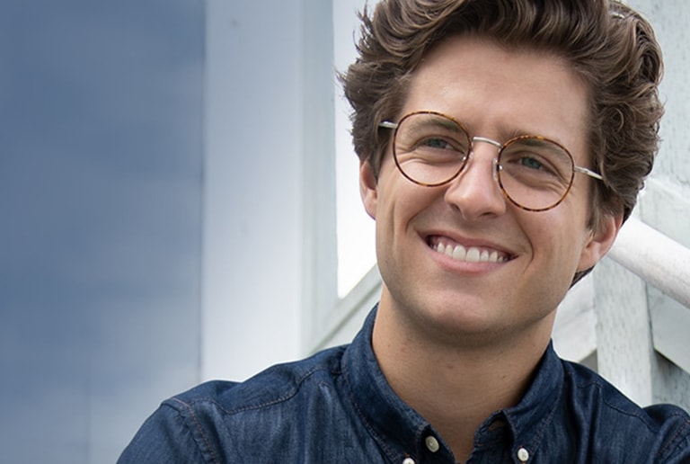 Man with brown hair is outside wearing round tortoiseshell glasses #7814325 with a chambray shirt.