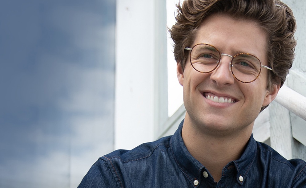 Man with brown hair is outside wearing round tortoiseshell glasses #7814325 with a chambray shirt.