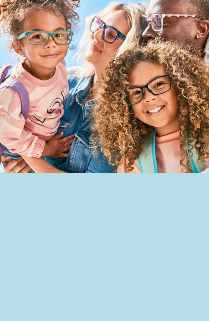 Smiling family with toddler wearing blue and yellow rectangle glasses, mom with purple and blue patterned glasses, dad with transparent glasses, and child with black rectangle glasses.