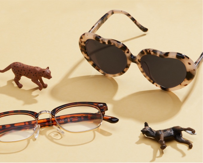 Image of two pairs of zenni glasses against a yellow background, with kids animal toys around them.
