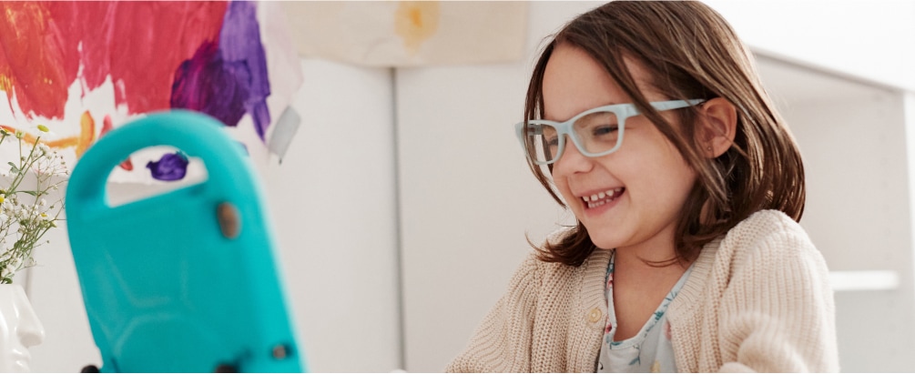 Image of a little girl wearing zenni glasses while drawing and watching a tablet.