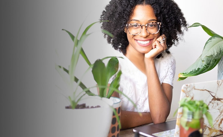 Image of a woman wearing Zenni ivory tortoiseshell square glasses #7815335 sitting by a desk with a laptop surrounded by plants.
