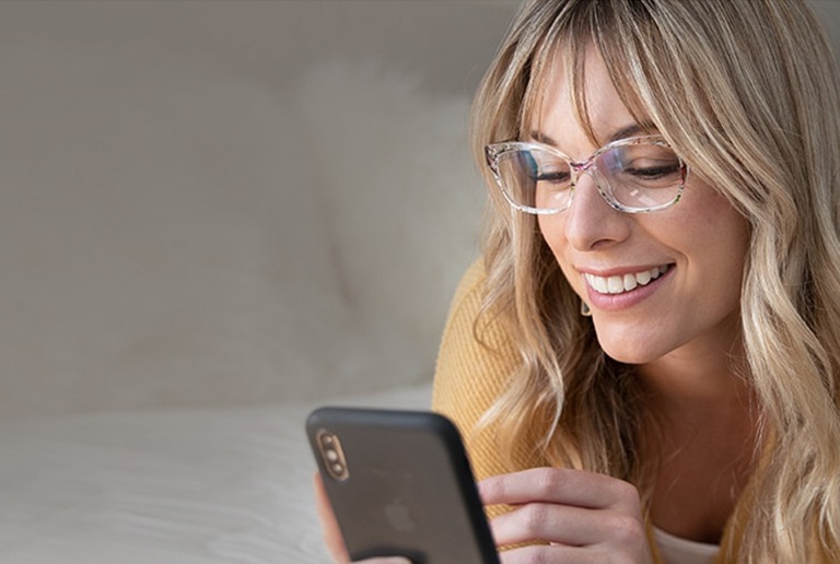 Woman with blond hair uses her iPhone while wearing translucent floral cat-eye glasses # 2018723.