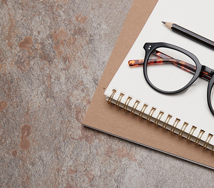 Spree round acetate glasses #4432921 from the Timo x Zenni Out of Office collection in black with tortoiseshell temple arms folded on top of a spiral-bound notebook with pencil.