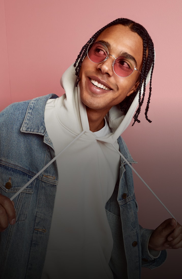 A happy couple, man with braids and woman with curly hair, both wearing Zenni FL-41 rose-tinted glasses and denim attire.