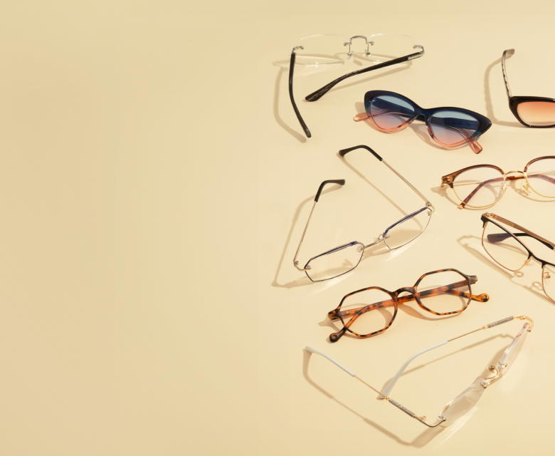 Several pairs of glasses and sunglasses resting on a beige background.