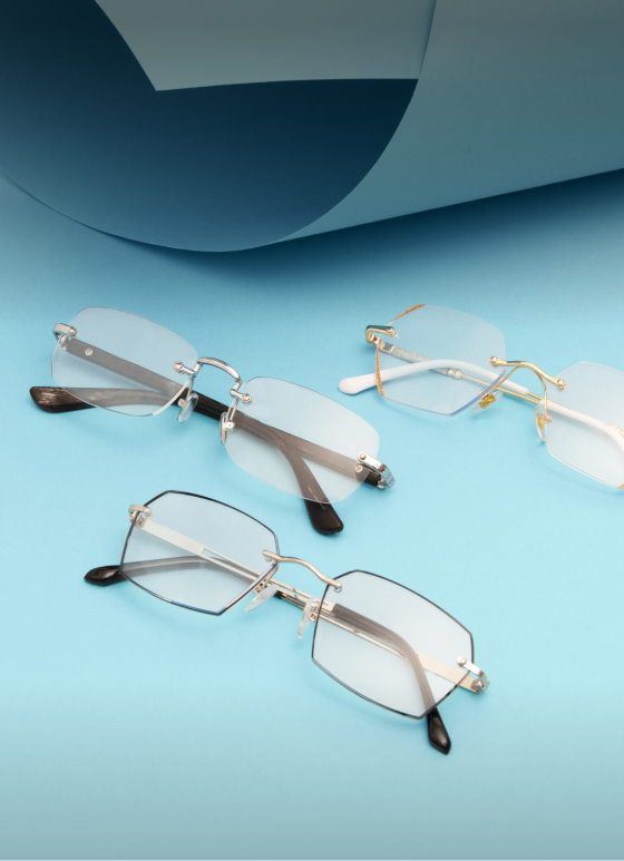 Three pairs of lightweight metal and rimless reading glasses on a light blue background.