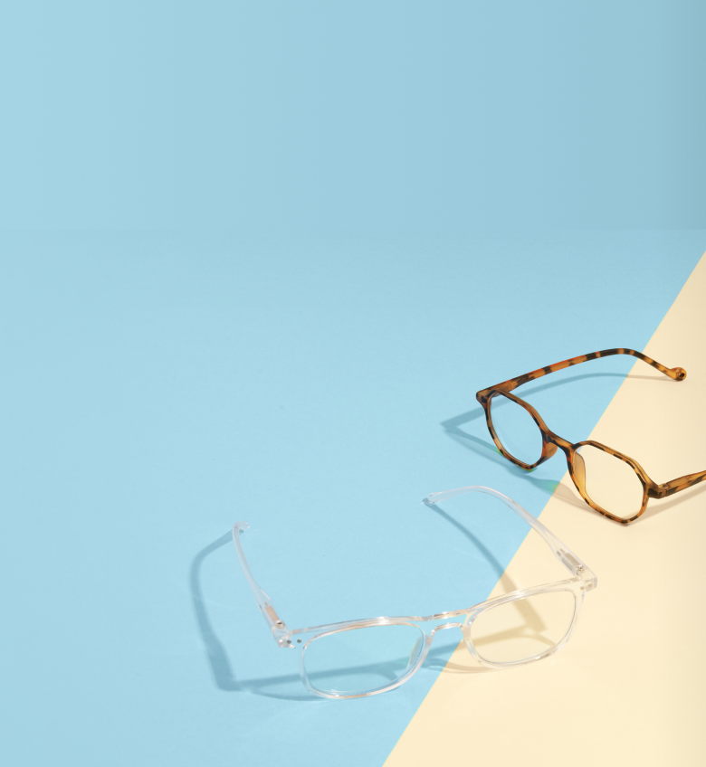 Tortoiseshell and clear frame reading glasses resting on a light blue and beige background.