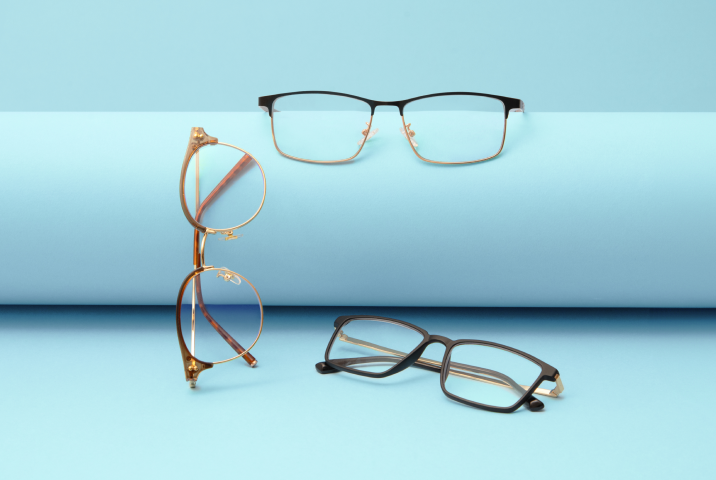 Three pairs of reading glasses resting on a roll of paper on a light blue background.