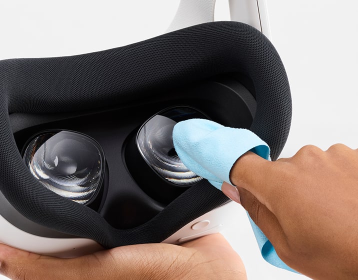 Close-up of a finger cleaning VR lenses inside a Meta Quest headset with a blue microfiber cloth.