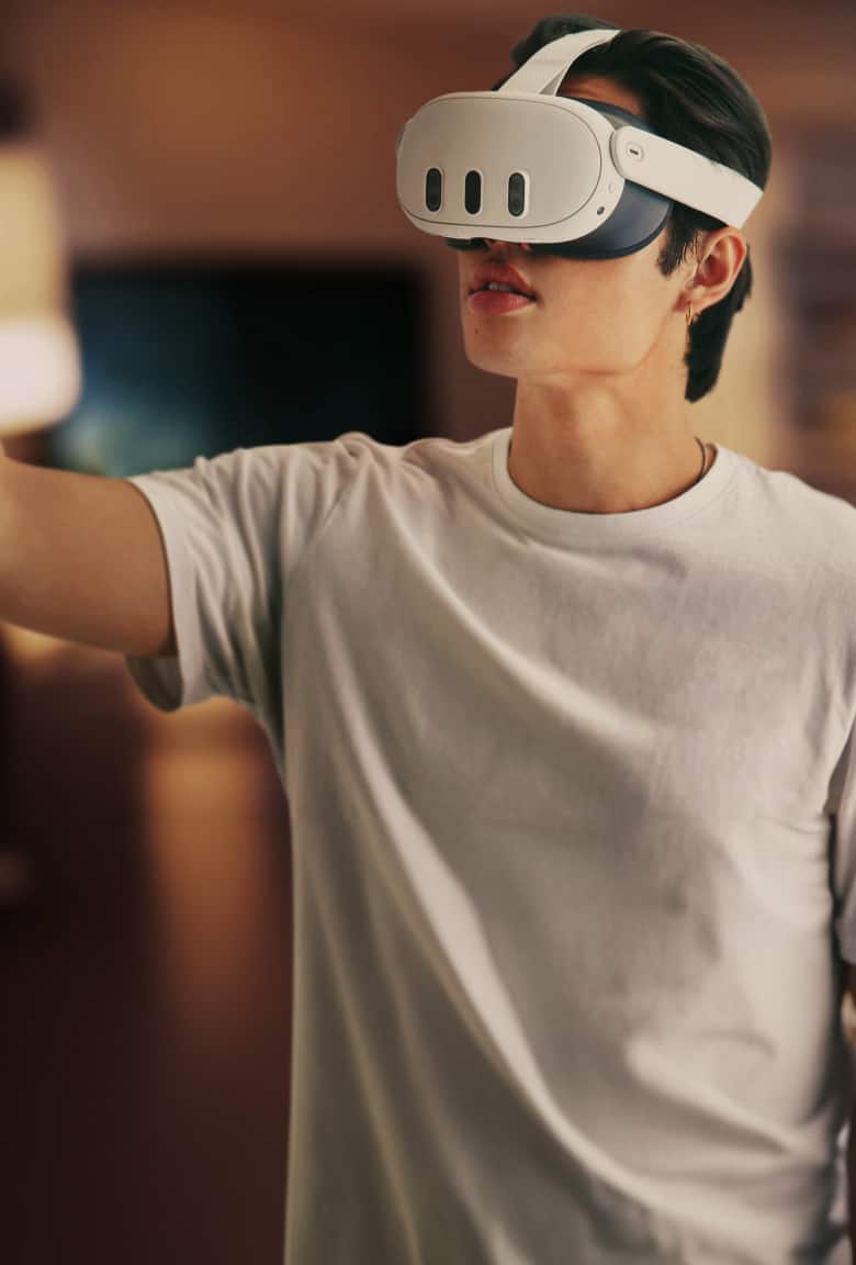 Person with black hair wearing a Meta Quest 3 VR headset over their face and holding a hand controller in their right hand.