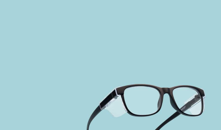 Gafas de seguridad Zenni de color negro con protectores laterales transparentes sobre fondo color azul claro.