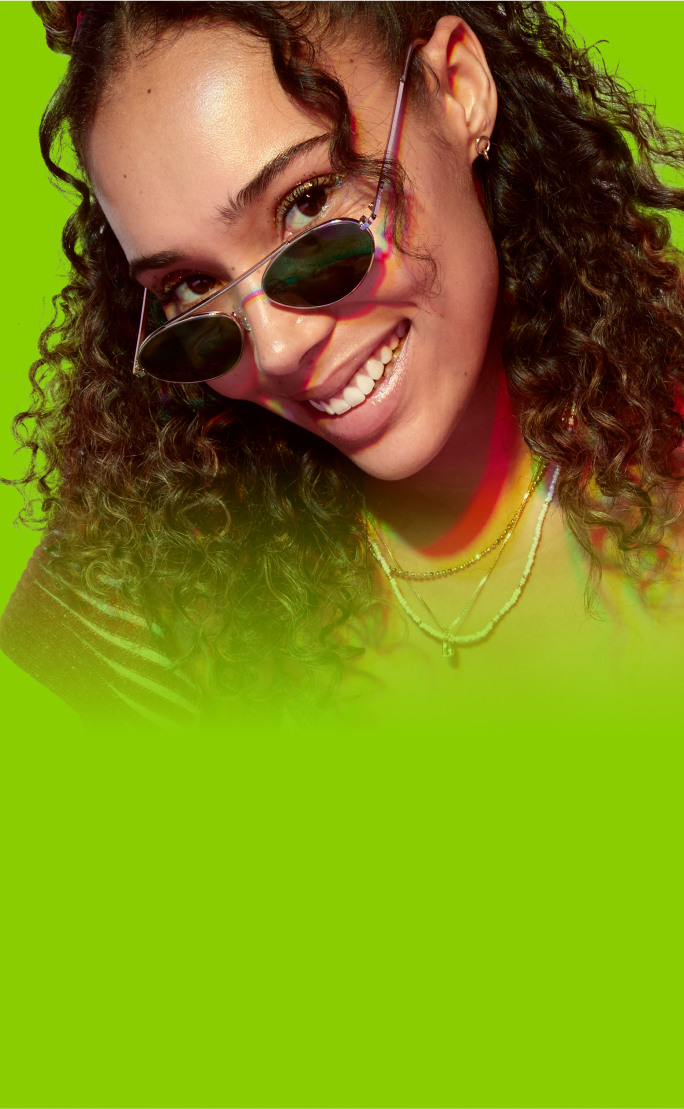 A young woman with curly hair wearing stylish, small, tinted glasses against a vibrant lime green background.